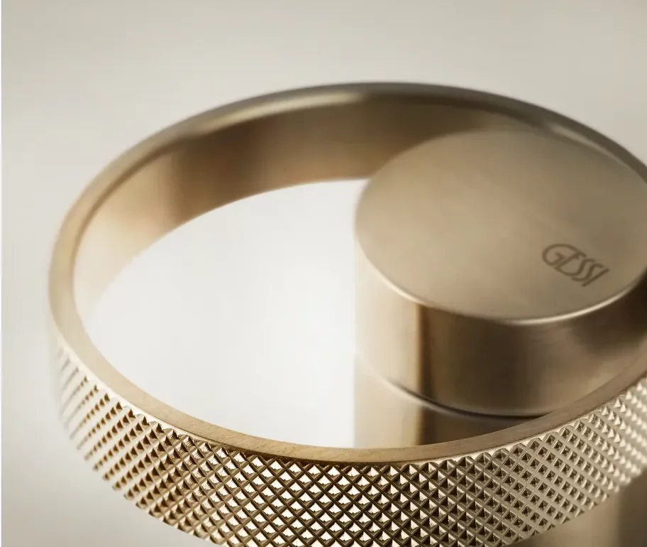 Close-up of a Gessi faucet handle in brushed brass with a knurled diamond-pattern ring